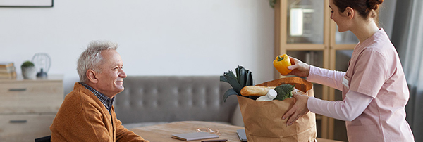 Carer unpacking groceries for senior man