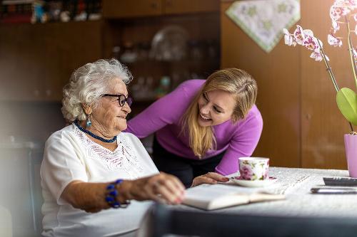 Elderly woman at table smiling with young woman carer